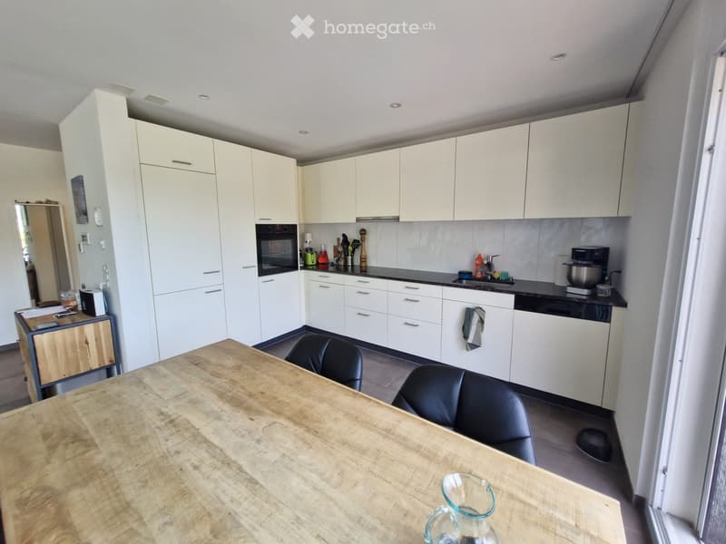 Modern kitchen with white cabinets, black countertops, and a wooden dining table with two black chairs.
