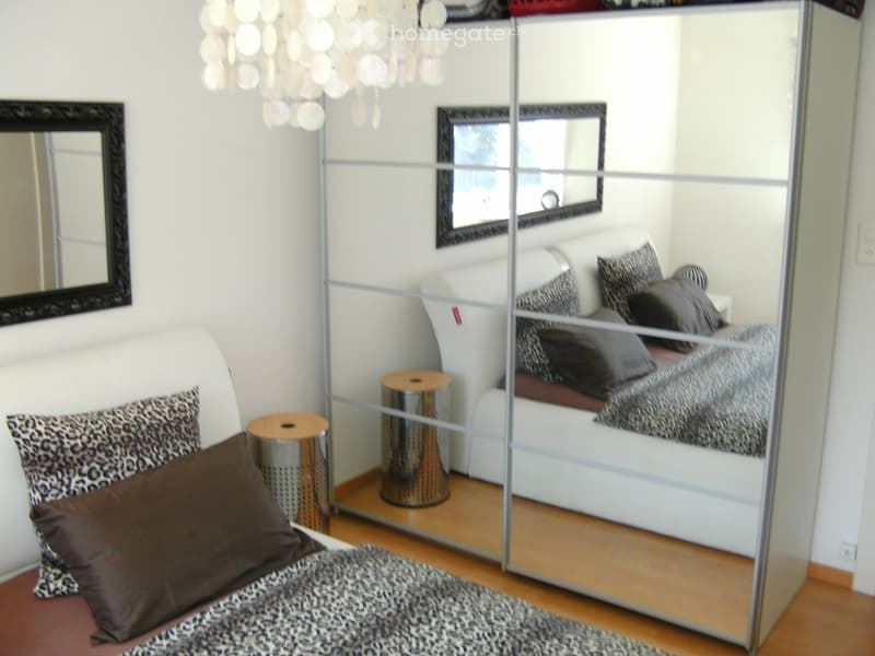 Modern bedroom with a white bed, leopard print pillows, a large mirror, and a chandelier.