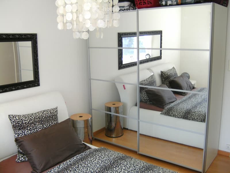 Modern bedroom with a white sofa, bed, leopard print pillows, a large mirror, and a stylish chandelier.