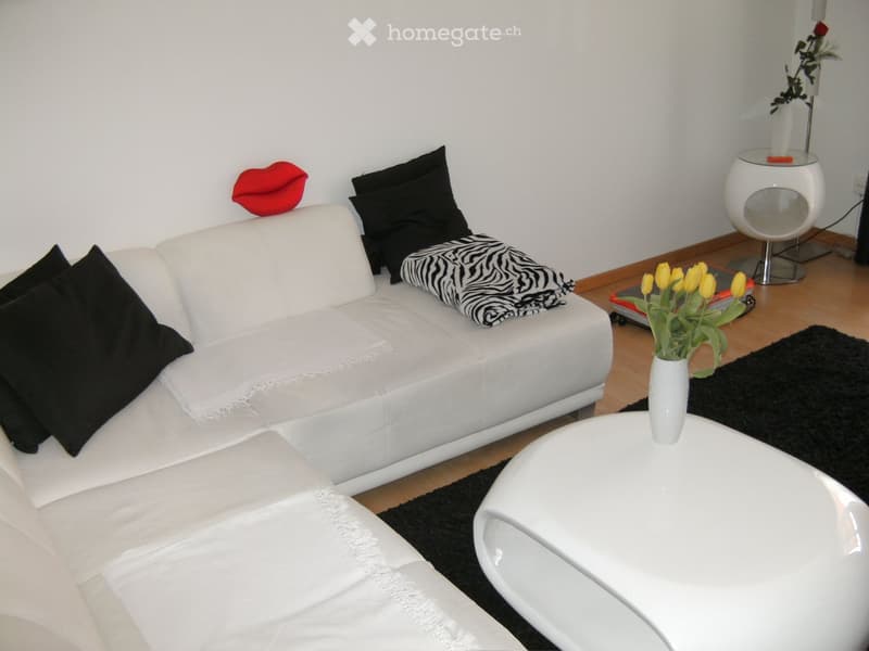 Modern living room with white leather sofa, black pillows, zebra throw, white coffee table, vase with yellow tulips, and a round white stool.