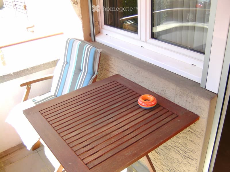 Balcony with a wooden table and a striped chair, a small decorative ring on the table.