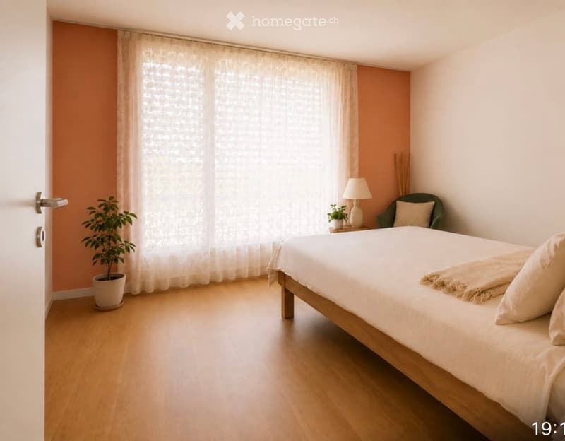 Bright bedroom with wooden flooring, large window with sheer curtains, bed with white linens, nightstand with lamp, small green armchair, and potted plants.