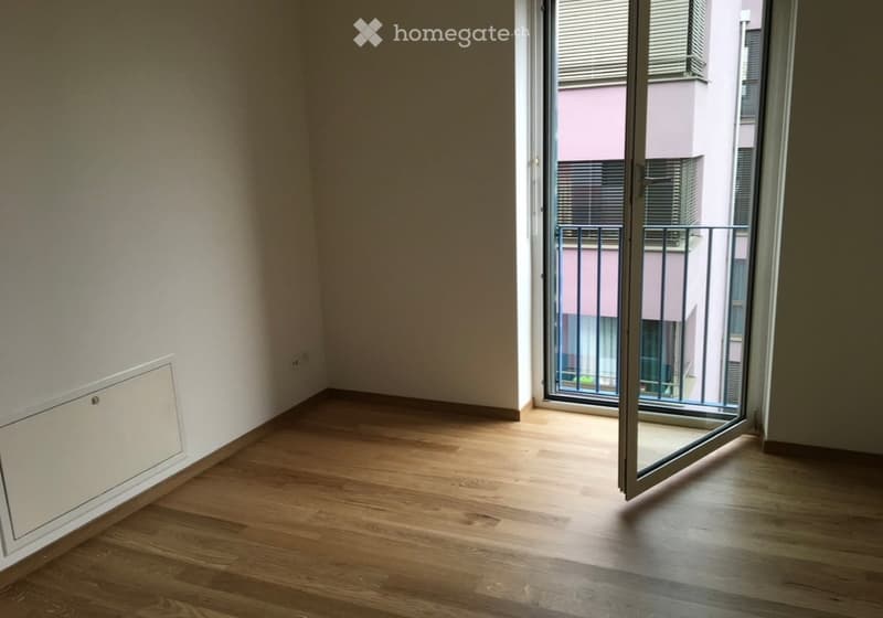 Empty room with wooden flooring, white walls, and a large sliding glass door leading to a balcony.
