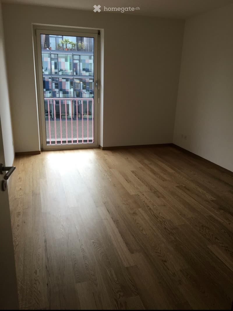 Empty room with light wooden flooring and a sliding glass door leading to a balcony.