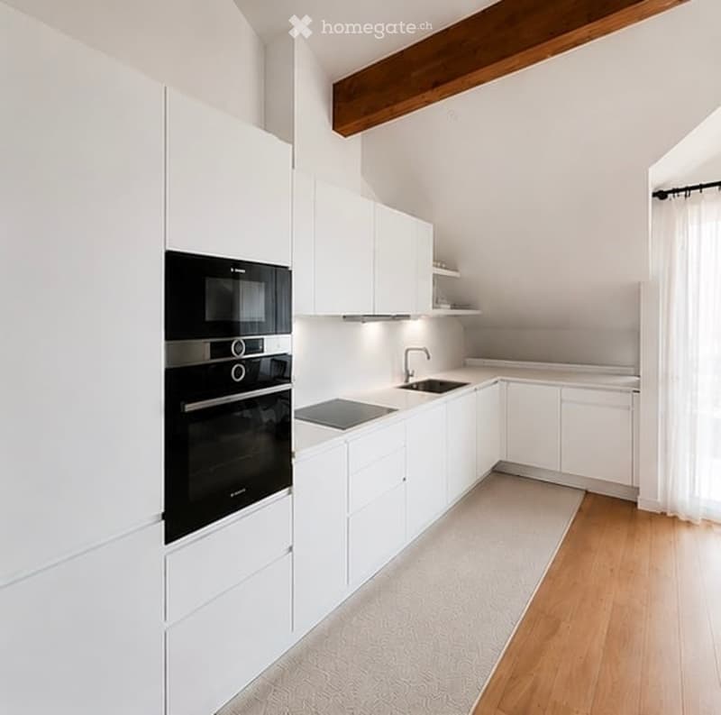 Modern kitchen with white cabinets, stainless steel oven, sink, and faucet. Light wood flooring and a small rug.