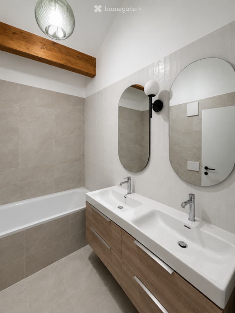 Modern bathroom with a double sink vanity, bathtub, large mirrors, and sleek lighting fixtures.