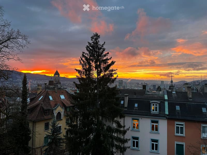 A cityscape view at sunset with multiple residential buildings, trees, and a distant skyline.