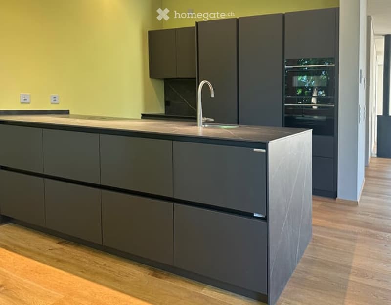 Modern kitchen with dark grey cabinets, a central island, and a sleek faucet. The walls are painted in a bright yellow color, and the floor is made of light wood.