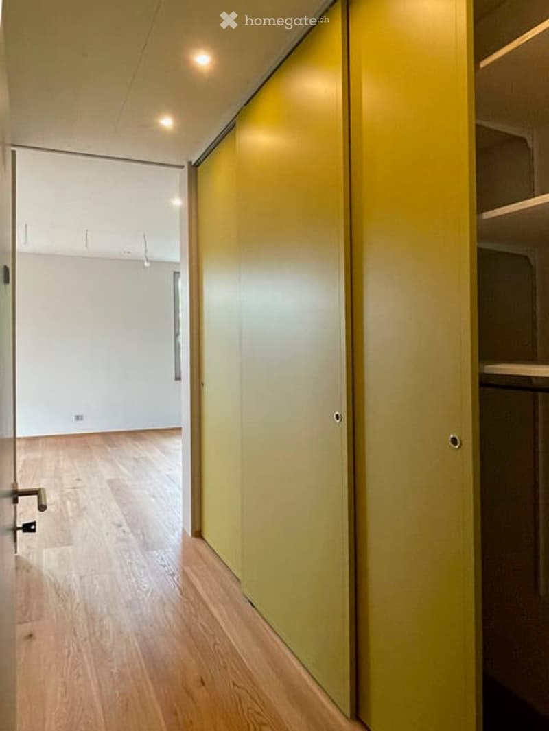 Empty room with light wooden flooring, white walls, and a closed yellow door. No furniture or equipment is present.