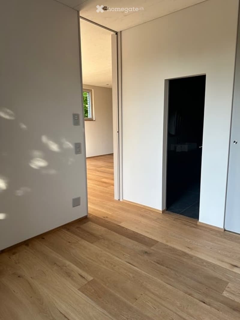 Empty room with light wooden flooring, white walls, and a large window letting in natural light. No furniture or equipment is present.