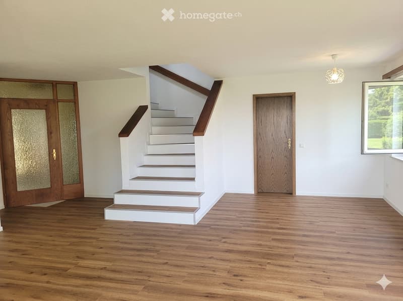 Empty room with wooden flooring, white walls, staircase leading to an upper level, and large windows with frosted glass panels.