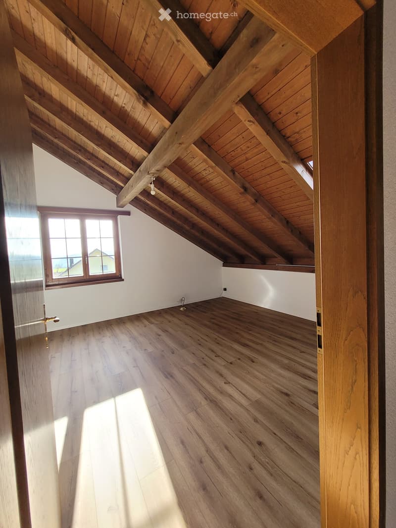 Empty attic space with exposed wooden beams, wooden flooring, and a single window letting in natural light.