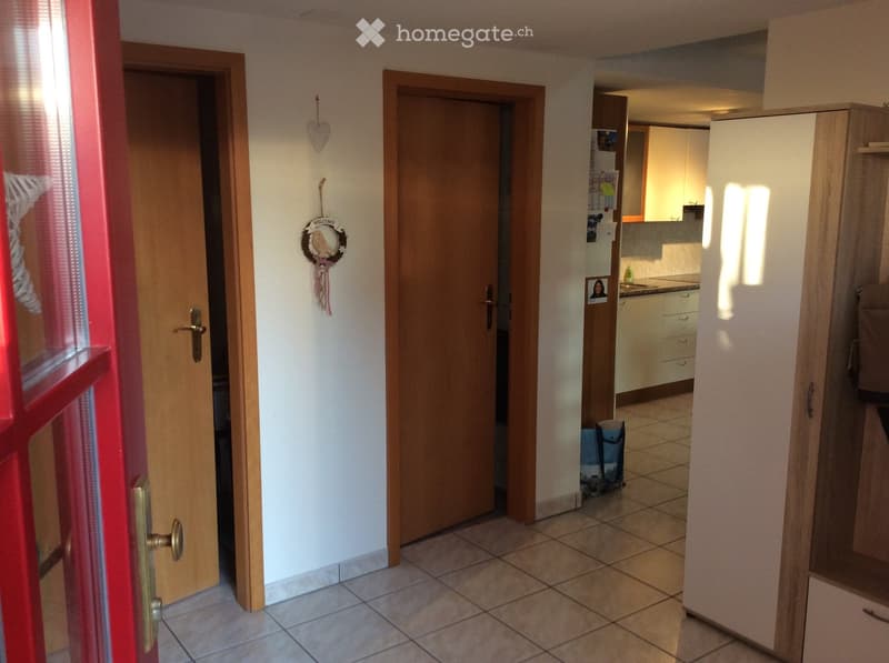Hallway with tiled floor, two wooden doors, and a view into a kitchen area with cabinets and a sink.