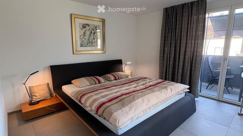 Modern bedroom with a large bed, nightstand, lamp, and a sliding glass door leading to a balcony.