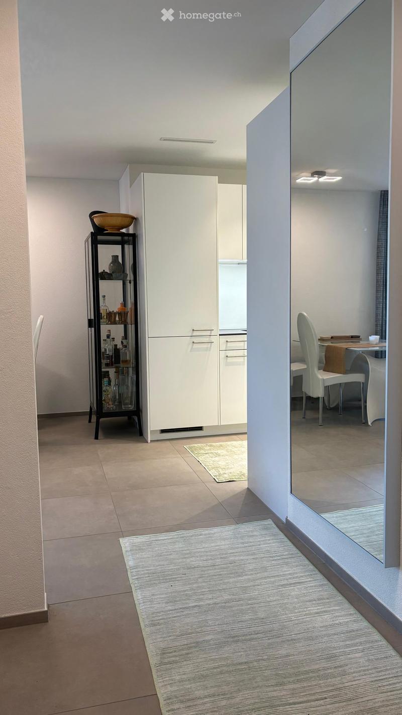 Modern, minimalist room with a white cabinet, a glass shelf with decorative items, a small table with chairs, and two rugs on the floor.