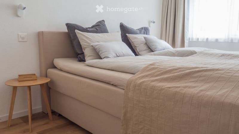 A modern bedroom with a neatly made bed, pillows, a wooden nightstand, and a small wooden tray on top.