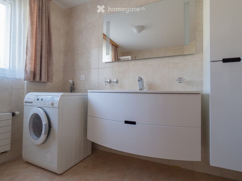 Modern bathroom with a white sink cabinet, mirror, washing machine, and tiled walls.