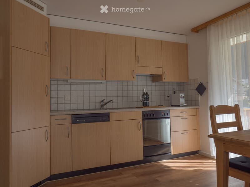 Modern kitchen with light wooden cabinets, stainless steel appliances, and a wooden dining table with a chair.