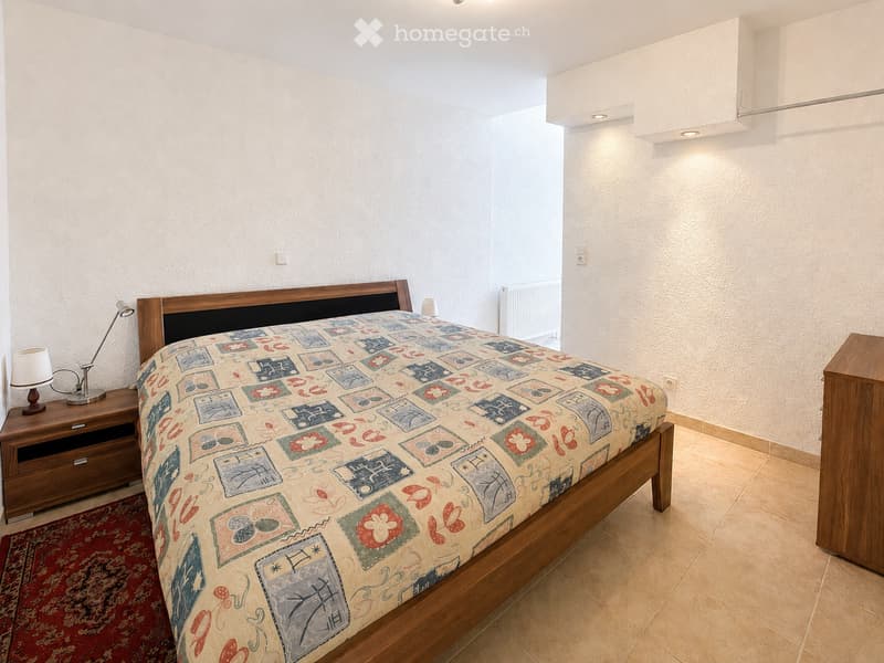 Cozy bedroom with a wooden bed, colorful patterned bedspread, nightstand with lamp, and a small table lamp on the floor.