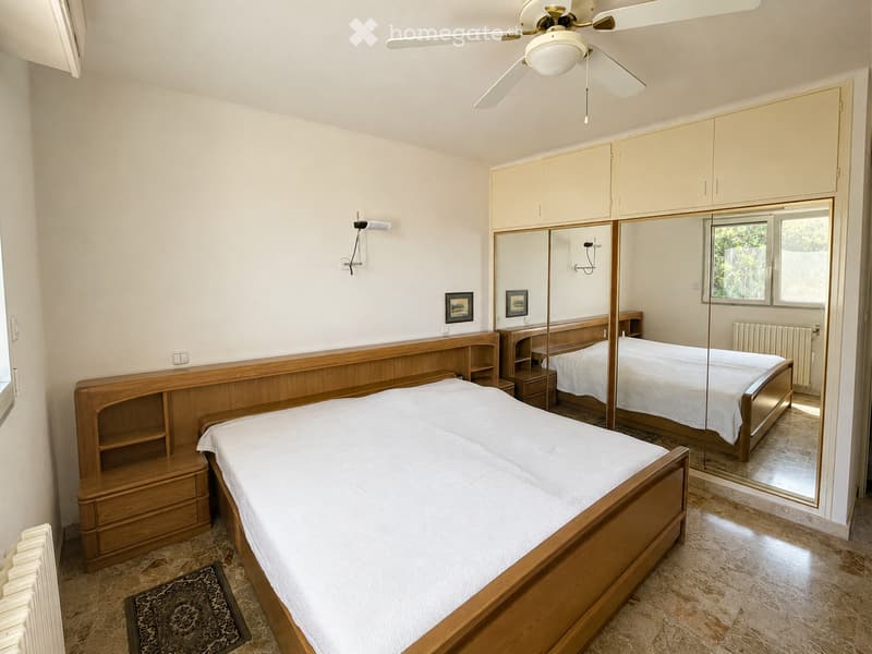 Spacious bedroom with two single beds, wooden furniture, large mirror, built-in wardrobes, and ceiling fan.
