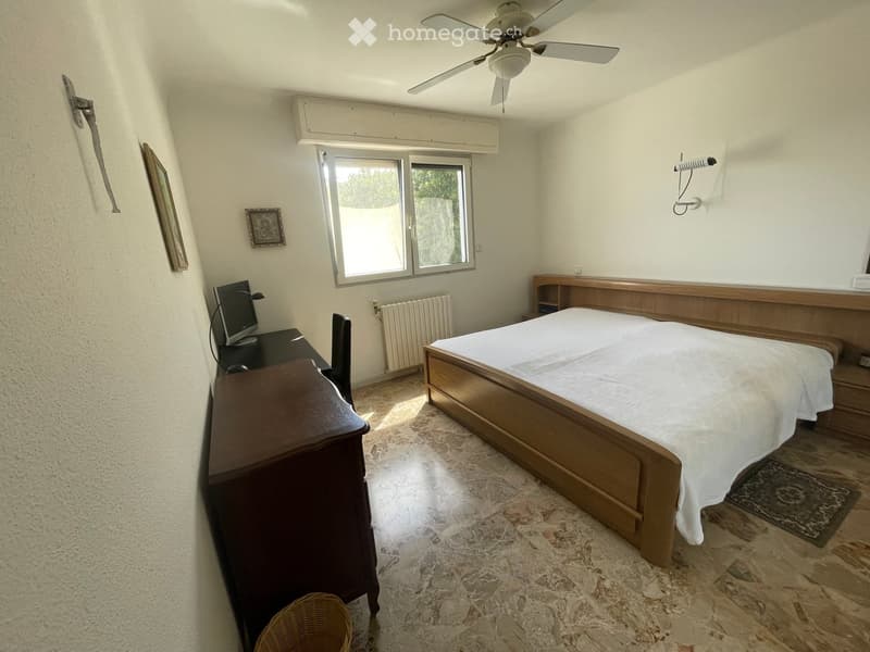 Bedroom with a wooden bed, desk with a computer monitor, chair, radiator, framed picture, and wicker basket on the floor.