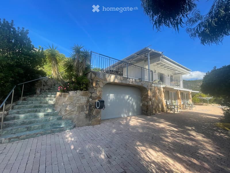 Two-story house with a stone facade, garage, outdoor patio, and staircase leading to an upper terrace.