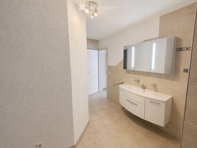 Modern bathroom with beige tiles, white sink cabinet, large mirror, and recessed lighting.