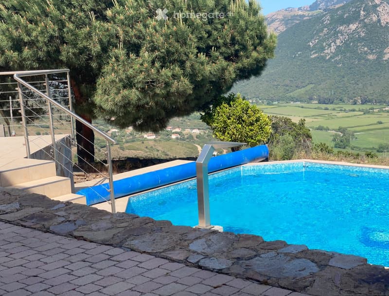 Outdoor swimming pool with a scenic mountain and valley view, surrounded by trees and greenery.