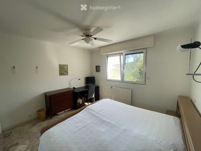 Bedroom with a bed, desk, chair, computer, lamp, radiator, picture frame, fan, and chest of drawers.