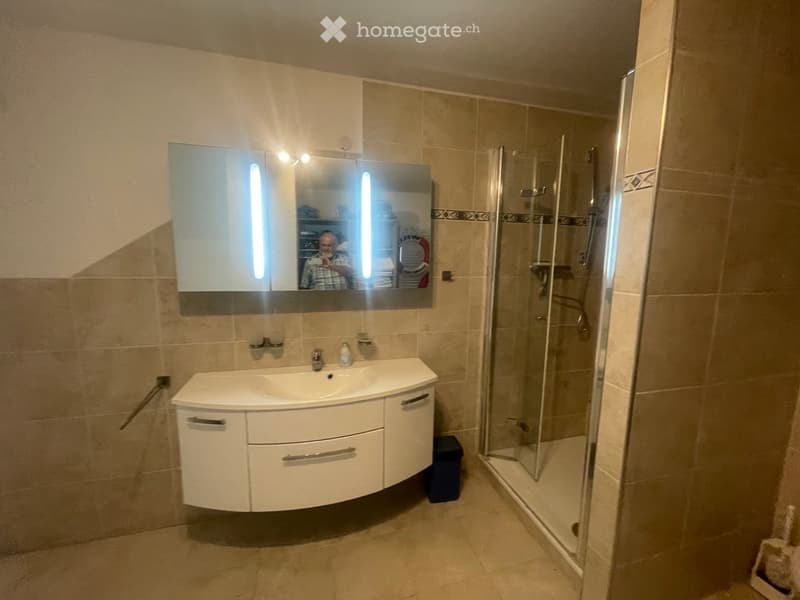Modern bathroom with a white sink cabinet, a large mirror with built-in lighting, and a glass-enclosed shower stall.