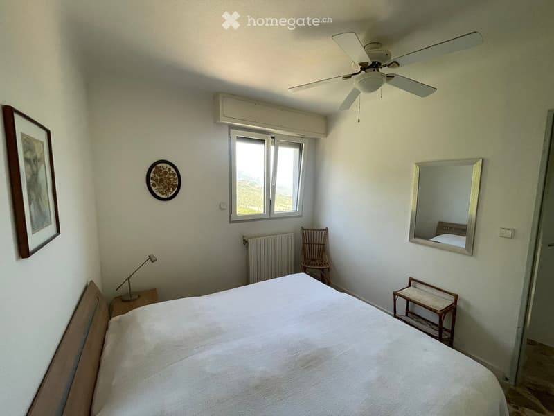 Cozy bedroom with a large bed, nightstand, chair, mirror, table lamp, radiator, and picture frame on the wall.