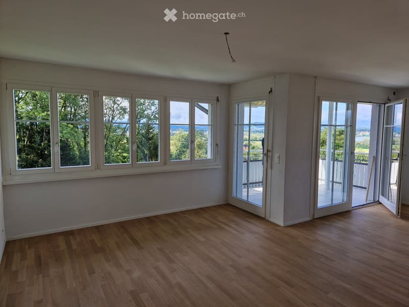 Empty room with wooden flooring, large windows, and sliding glass doors leading to a balcony.