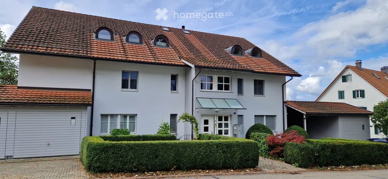 Two-story house with red-tiled roof, white exterior, multiple windows, garage, and well-maintained garden.