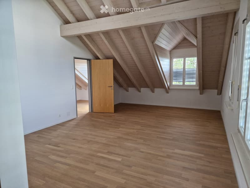 Empty attic room with wooden floors, white walls, exposed wooden beams, and a skylight window.