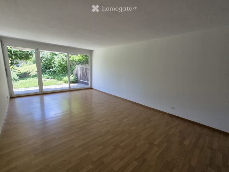 Empty room with wooden flooring and large sliding glass doors leading to a garden area.