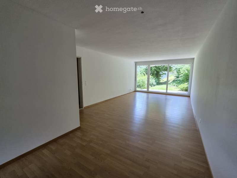 Empty room with wooden flooring, white walls, and large windows letting in natural light.
