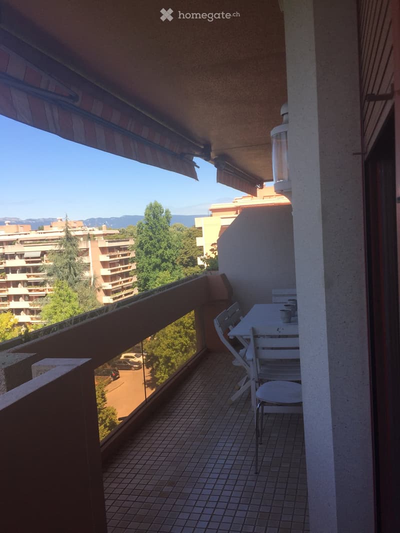 Balcony with tiled floor, table, and chairs, overlooking a cityscape with trees and buildings.