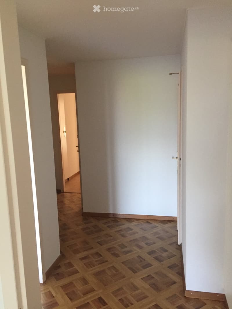 Empty hallway with wooden flooring and white walls, featuring two doors and a visible room at the end.