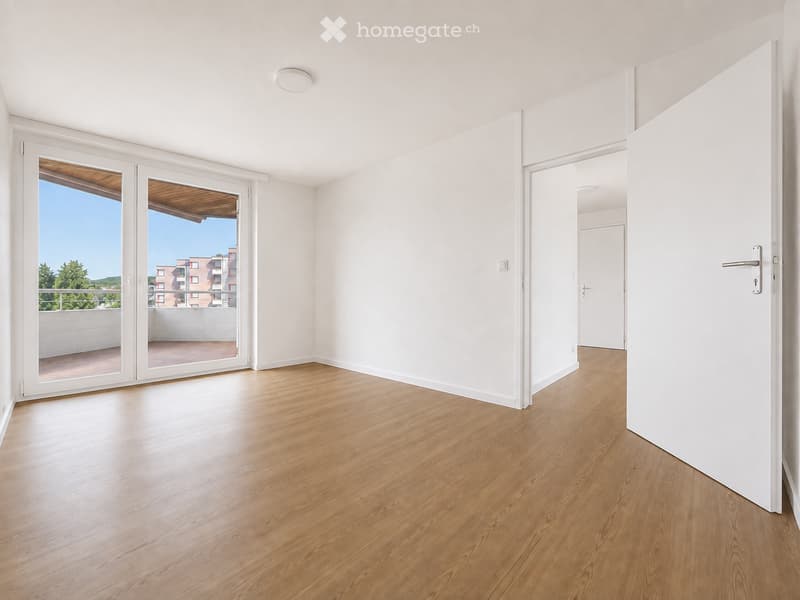 Empty room with light wooden flooring, white walls, and large sliding glass doors leading to a balcony or terrace.