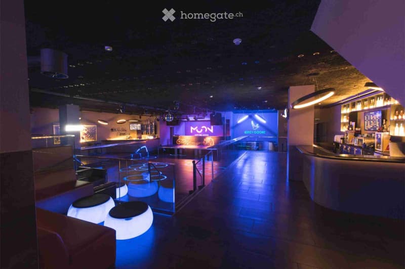 A modern, illuminated lounge with a bar, seating area, and illuminated stools