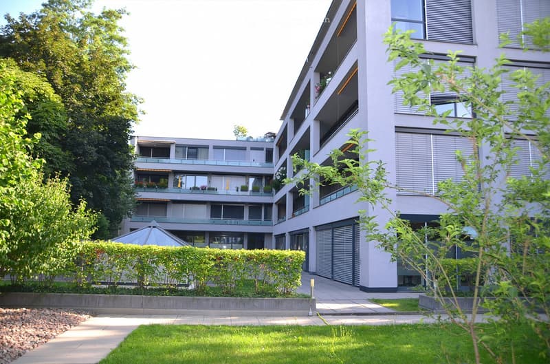 Modern multi-story residential building with balconies, surrounded by greenery and a well-maintained lawn.