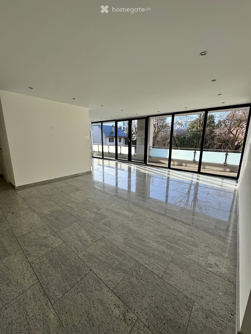 Empty room with polished marble tiles, large glass sliding doors leading to a balcony, and recessed ceiling lighting.