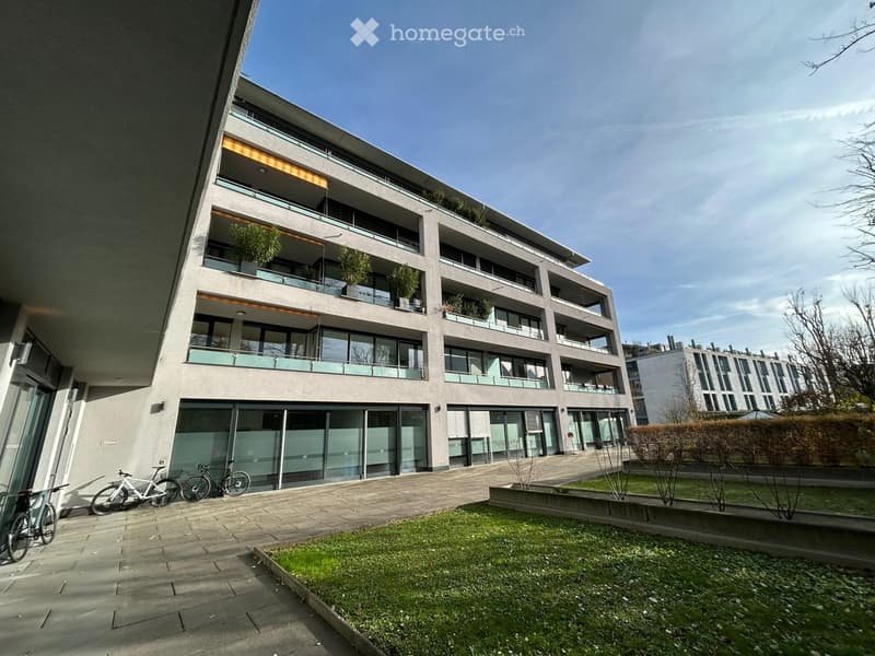 Modern multi-story residential building with balconies, large windows, and a landscaped courtyard area with bicycles parked nearby.