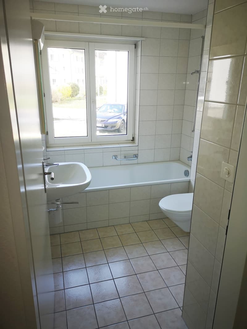 modern bathroom with sink, bathtub, toilet, and window overlooking a parking area