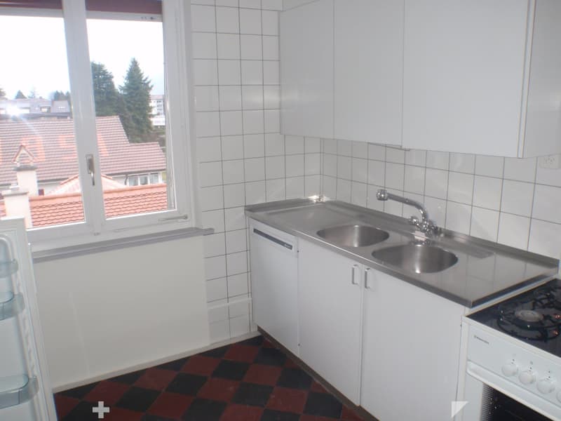 A small kitchen with white tiled walls, a stainless steel sink, a gas stove, and white cabinets.
