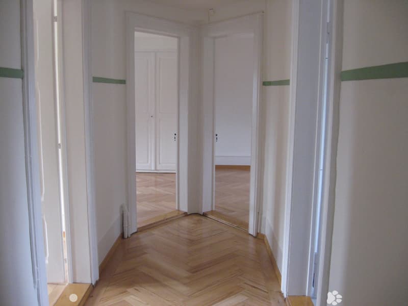Empty hallway with wooden flooring and white walls, featuring multiple doors leading to other rooms.