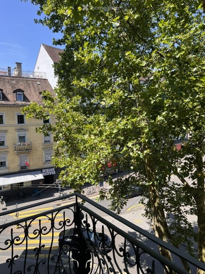 Balcony overlooking a street with trees, buildings, and a restaurant sign visible.