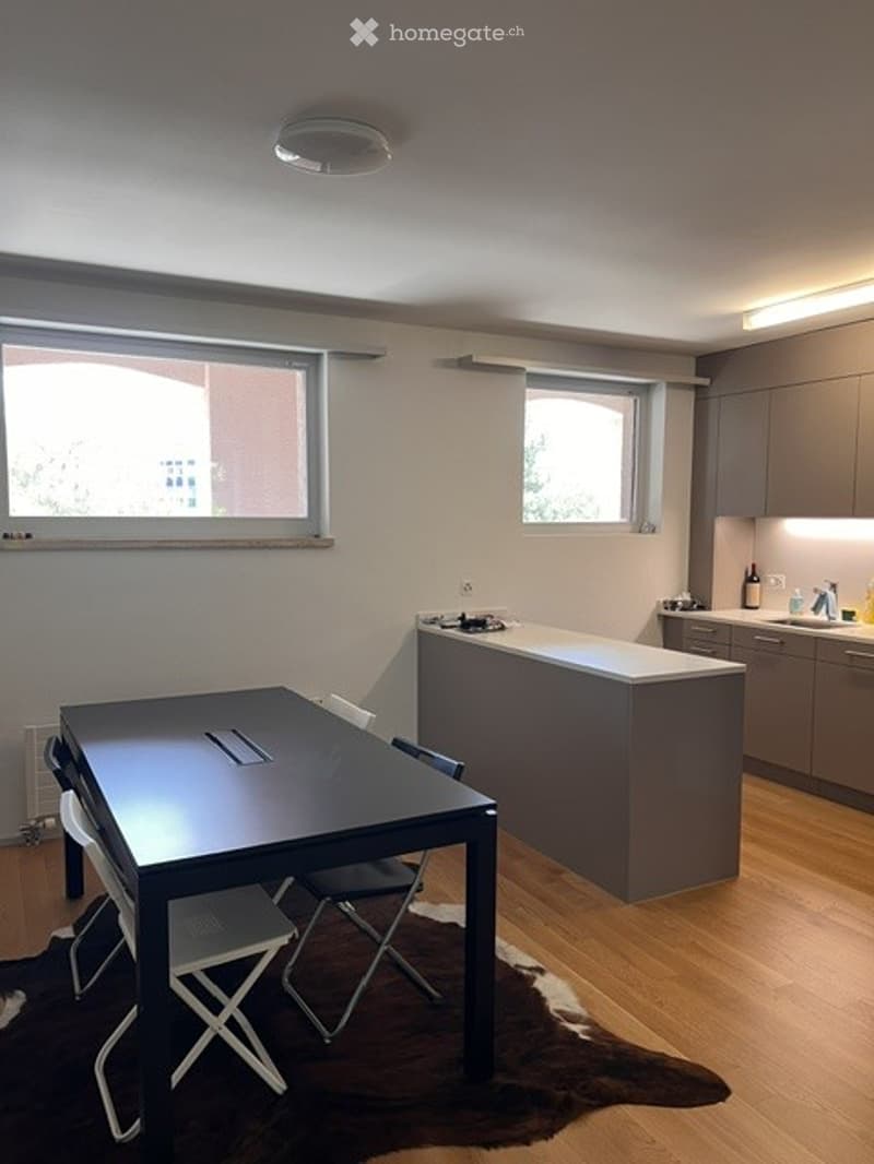 Modern open-plan kitchen and dining area with light grey cabinets, a white countertop kitchen island, a black dining table with four chairs, and a wooden floor.