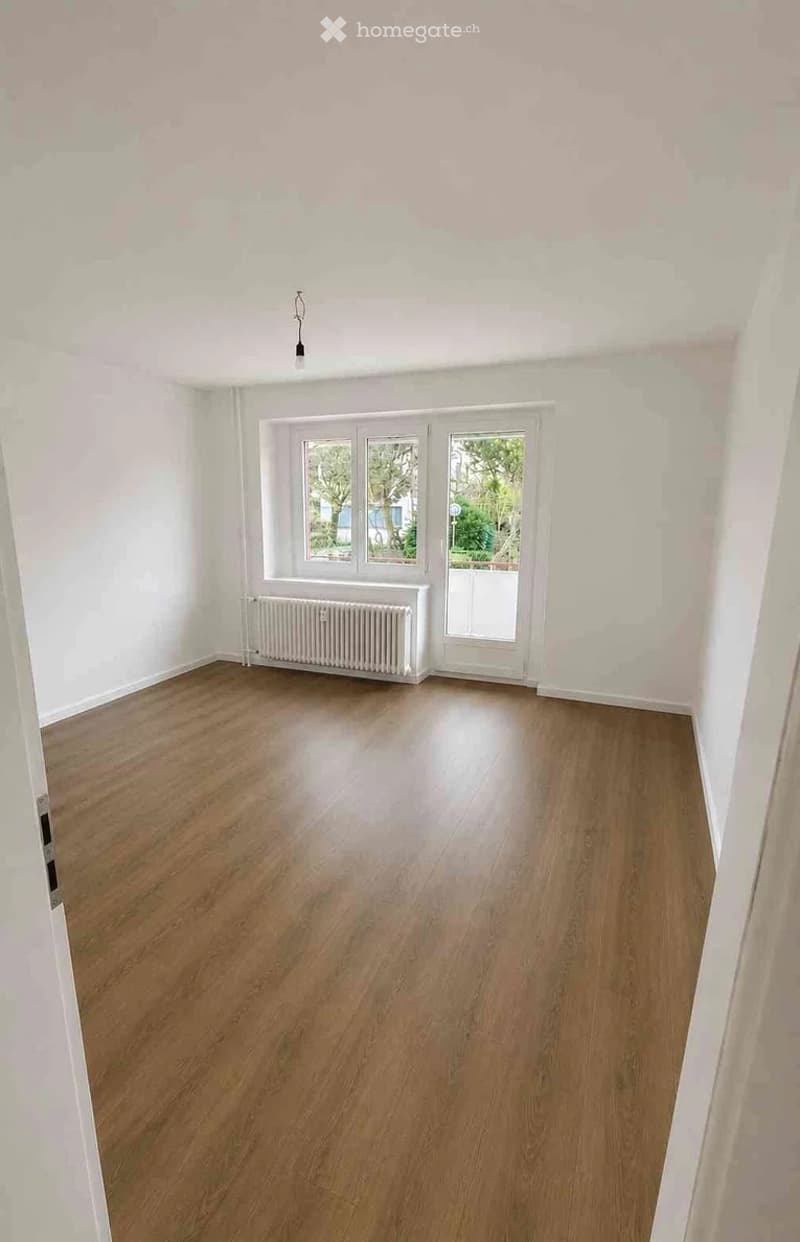 Empty room with wooden flooring, white walls, and a radiator under a window. No furniture or equipment present.