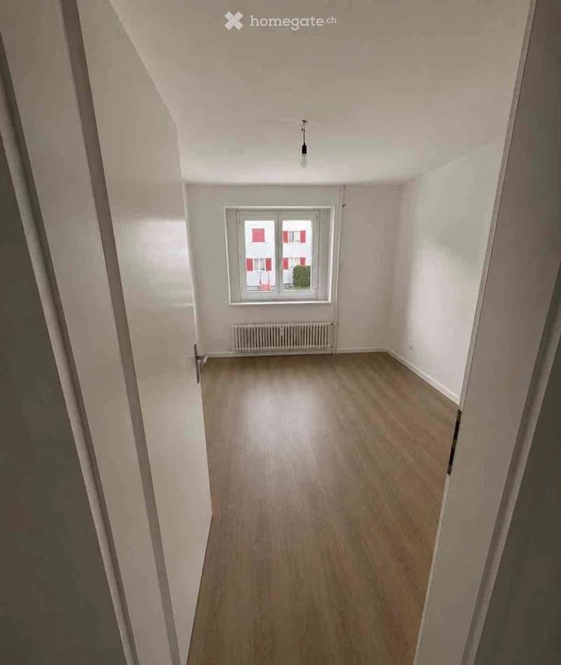 Empty room with wooden flooring, white walls, a single window, and a radiator below it. No furniture or personal items are present.